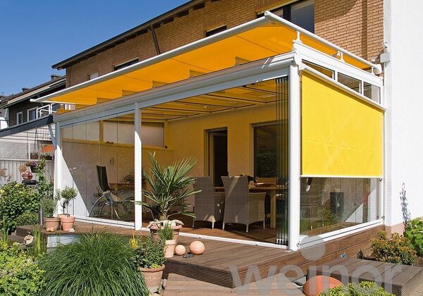 Moderne Terrassenüberdachung mit gelber Markise und Glaswänden an einem Einfamilienhaus.