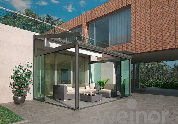 Moderner Wintergarten mit Glasdach und Loungemöbeln an einem Haus mit Klinkerfassade.