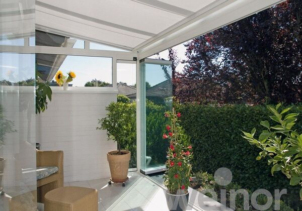Moderner Wintergarten mit Glas-Schiebetür, gemütlicher Sitzgruppe und Blick in den Garten.