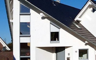 Modernes Einfamilienhaus mit Satteldach, weißen Fassaden und großen Fenstern bei Sonnenschein.