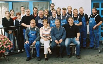 Gruppenfoto eines Handwerker-Teams vor einem Gebäude mit blauen Fenstern und Türen.